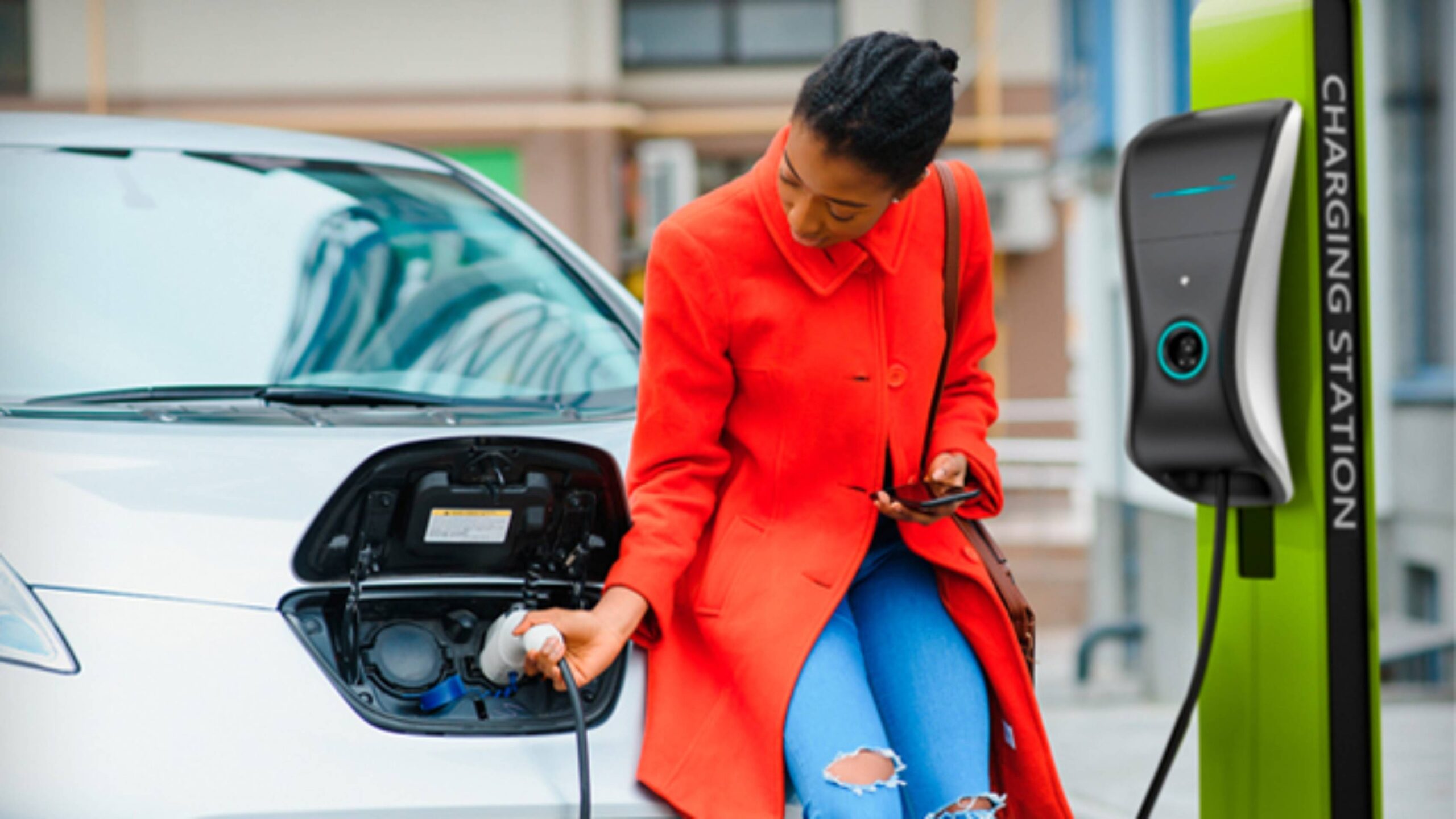 A person in a bright red coat is charging an electric vehicle.